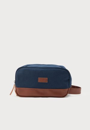 Toaletna torbica od plavog platna i smeđe kože s patentnim zatvaračem i bočnom ručkom, pravokutnog oblika, s naljepnicom "JACK & JONES" u središtu sprijeda.