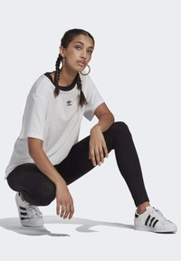 Vit bomullströja med svart rund hals och liten Adidas-logotyp, matchad med svarta leggings och klassiska vita sneakers med svarta ränder.