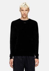 Maglione nero a maniche lunghe con scollo rotondo e tessuto testurizzato. Presenta un piccolo accento metallico circolare sul petto.