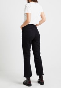 Svarta högmidjade jeans med rak benlängd, femfickorsdesign och subtila detaljer bak, tillsammans med en vit T-shirt med rundad hals.