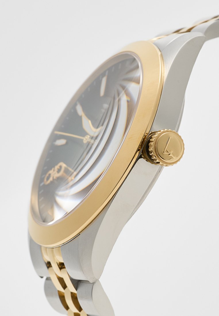 Montre argentée et dorée avec un boîtier rond, un cadran à motif sombre, trois aiguilles et une couronne texturée sur le côté. Bracelets en maillons métalliques.