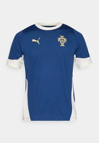 Blå sportströja med vita detaljer, korta ärmar och rund hals. Har en gul logotyp på bröstet och en texturerad tyg.