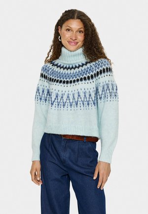 Pull en laine bleu clair avec un col montant. Présente un motif géométrique en bleu plus foncé et noir le long de l'encolure et du corps. Coupe courte.