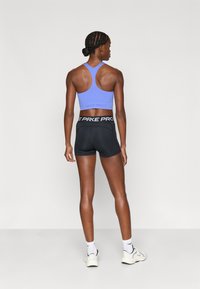 Αθλητικό σουτιέν σε ανοιχτό μωβ με στρογγυλή λαιμόκοψη και σχεδιασμό racerback, συνδυασμένο με μαύρο εφαρμοστό σορτς με λευκή ζώνη μέσης και εμφανές λογότυπο.