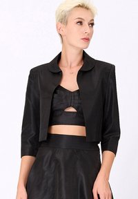 Veste noire cropped avec un col arrondi, des manches trois-quarts et une texture lisse, associée à un haut noir sans manches avec des découpes.