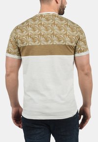 Kortærmet T-shirt med et brun- og hvidt palmeblad mønster på den øverste ryg, med en kontrasterende hvid nederste sektion og lys grå krave.