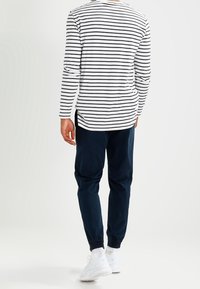 White long-sleeve shirt with black stripes, paired with navy jogger pants and white sneakers. Features a relaxed fit and elastic cuffs.