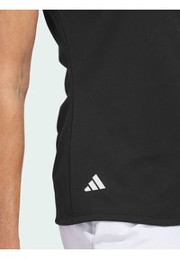 Černé sportovní tričko s hladkou texturou, s bílým akcentem loga Adidas v dolním levém rohu. Přiléhavý střih s kulatým lemem.