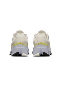 Zapatillas deportivas blancas con una parte superior lisa y acentos texturizados, con un logo visible en gris y una franja amarilla en contraste en el talón.