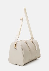Beige faux leather duffle bag with gold hardware, dual top handles, and a removable strap. Rounded shape with decorative stitching details.