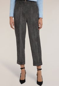 Grijze corduroybroek met verticale strepen, opgerolde manchetten en een getailleerde pasvorm, gecombineerd met zwarte puntige hakken en een blauw topje met stippen.