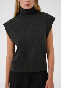 Tumši pelēks, bez piedurknēm turtlenecks džemperis ar brīvu piegriezumu, izgatavots no mīksta adījuma materiāla; tam ir augsts kakls un gluda tekstūra.