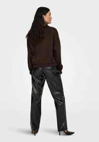 Bruine cropped sweatshirt met een ontspannen pasvorm, gecombineerd met glanzende zwarte nepleer broeken met een rechte snit en zijzakken.