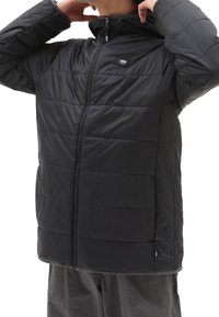Czarna ocieplana kurtka z zamkiem z przodu, pikowany fason i kaptur. Posiada małe logo i detale kieszeni po bokach. Gładka tekstura.