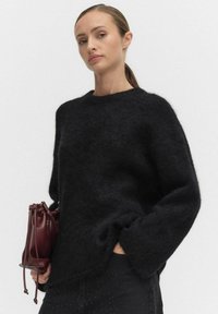 Svart, fluffig stickad tröja med bred halsringning och långa ärmar. Åtföljs av en liten, burgunderfärgad läderpåse med snörning på sidan.