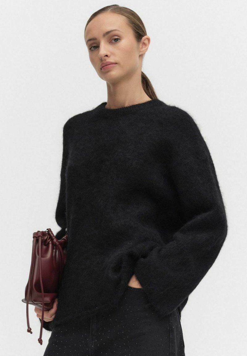 Svart, fluffig stickad tröja med bred halsringning och långa ärmar. Åtföljs av en liten, burgunderfärgad läderpåse med snörning på sidan.