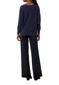 Navyblauer, übergroßer Pullover mit weitem Ausschnitt, gerippten Bündchen und einer Naht auf der Rückseite, kombiniert mit hochtaillierten, dunkelblauen, ausgestellten Jeans.