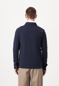 Navy blue polo jacket in soft fabric, featuring a collared neck and long sleeves. Plain design with minimal detailing and tailored fit.