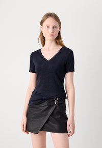 Haut à col en V bleu marine à manches courtes en tissu scintillant, associé à une jupe enveloppante en simili cuir noir avec des boucles en argent.
