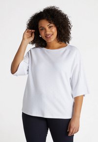 White top with short sleeves, featuring a round neckline and small dotted pattern. Soft fabric with a relaxed fit, paired with dark jeans.