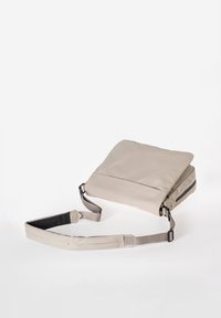 Lichtbeige crossbodytas met verstelbare schouderriem, zijvak met rits en zachte stoftextuur tegen een witte achtergrond.