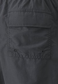 Pantaloni corti in nylon neri con una singola tasca posteriore con chiusura a bottone e vita arricciata. Leggeri e con una texture liscia.