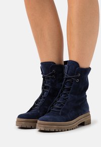 Bottines en suède bleu marine avec un devant à lacets, une tige texturée et une semelle en caoutchouc marron épaisse. Comprend des œillets pour les lacets et un col doux.