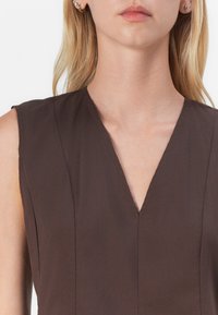 Brun ärmlös topp med V-ringning, subtila plisseringar och mjuk textur, vilket framhäver en minimalistisk design utan dekorationer.