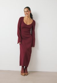 Burgundia soonikko kudum Dress, millel on sügava kaelus, pikad varrukad ja vormi järgiv siluett, koos sobivate saapikestega.