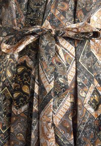 Patterned fabric dress featuring intricate paisley and geometric designs in black, orange, and cream tones, with a bow at the waist.