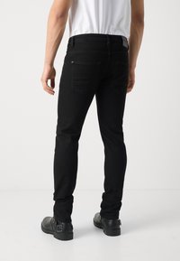 Jeans skinny negros con una textura suave, diseño de cinco bolsillos y una cintura alta. Combinados con botines negros.