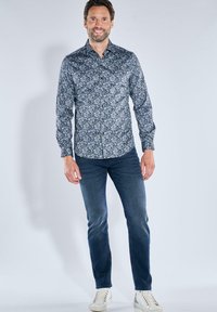 Blaues blumiges Hemd mit langen Ärmeln, aus Baumwolle, gemustertes Design, kombiniert mit dunklen Jeans und weißen Turnschuhen.
