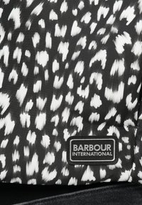 Μαύρο ύφασμα με λευκό αφηρημένο σχέδ�ιο· περιλαμβάνει ορθογώνια μαύρη ετικέτα με την επιγραφή "BARBOUR INTERNATIONAL" σε λευκό κείμενο.