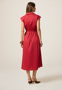 Rotes Kleid mit kurzen Ärmeln, tailliertem Gürtel und einer Länge bis zur Mitte der Wade. Glattes Material mit Kragen und lockerem Schnitt.