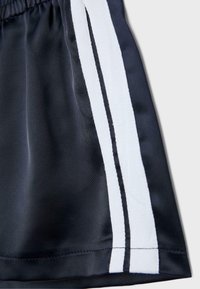 Gros plan d’un short en tissu noir avec une ceinture élastique et deux bandes blanches verticales sur le côté.