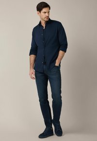 Granatowa koszula z guzikami, ciemne dżinsy i granatowe trampki. Slim fit. Koszula ma długie rękawy i klasyczny kołnierzyk. Miękka faktura. Prosty design.