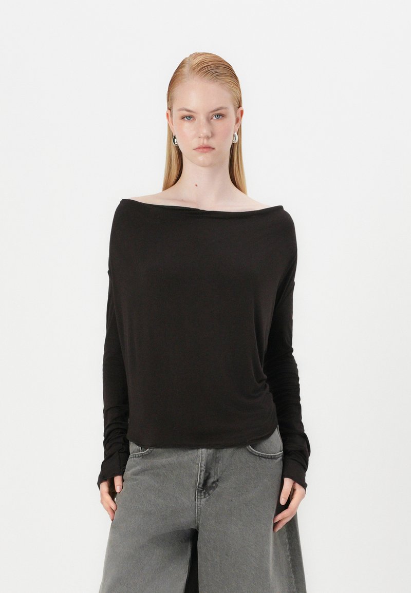 Haut noir à épaules dénudées à manches longues en tissu doux, doté d'une coupe décontractée et de poignets côtelés, associé à un pantalon large gris.