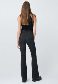 Jeans noires taille haute évasés avec une texture denim lisse, poches arrière et une coupe ajustée. Associés à un haut sans manches noir.