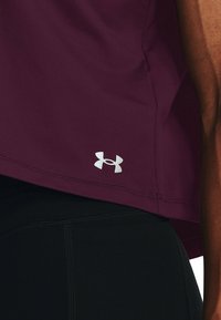 Vinröd sporttopp med avslappnad passform, med en silverfärgad Under Armour-logotyp vid fållen. Tillverkad av mjukt, flexibelt tyg utan synliga mönster.