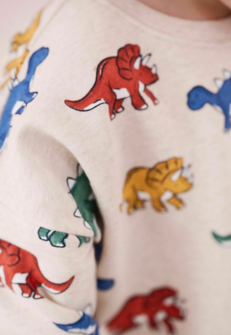 Sweatshirt beige avec des motifs de dinosaures colorés en bleu, rouge, vert et jaune. Matériau doux avec une coupe décontractée.