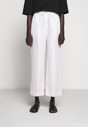 Pantalones palazzo de color rosa claro con cintura elástica y cordón, que presentan una textura suave y dobladillos acampanados, combinados con sandalias negras.
