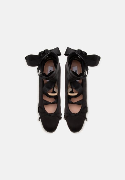 Paire de ballerines noires avec des liens ruban autour de la cheville, bouts arrondis et semelles intérieures douces, vues de dessus sur fond blanc.