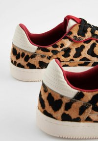 Sneakers con stampa leopardata, dalla texture morbida, lacci neri, dettagli rossi e punte di tacco color crema, dotati di una suola in gomma.