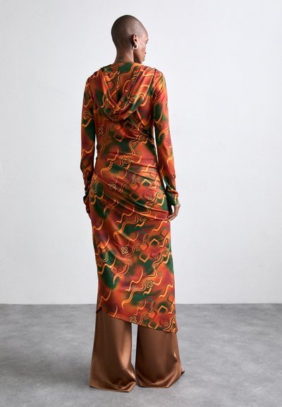 Hooded dress in vibrant orange, green, and red with swirling patterns, paired with silky brown wide-leg pants, shown from the back.