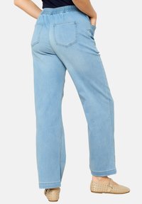 Pantalones de mezclilla de color azul claro con corte relajado, cinturilla elástica, dos bolsillos traseros y puños enrollados, combinados con bailarinas beige con tachuelas.