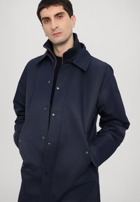 Navy blue waterproof coat with a button front, pointed collar, and side pockets. Smooth texture with subtle sheen.