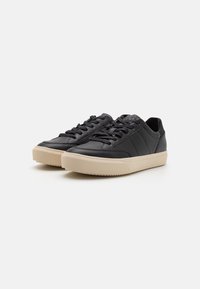 Svarte lær-sneakers med lav profil, rund tå og teksturert kremfarget gummisåle. Har svarte snørebånd og subtile søm-detaljer.