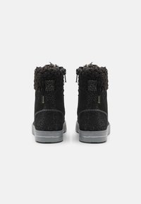 Botas de tobillo de ante negro con un cuello de piel de pelo texturizado negro, puntos plateados en el tacón y una suela de goma gris. Dos cremalleras en la parte posterior.