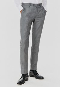 Szare spodnie w prążki o dopasowanym kroju, z płaskim przodem, kieszeniami bocznymi i zapięciem na guzik. Nosi się je z czarnymi butami wizytowymi.