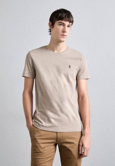 T-shirt en coton beige avec un col rond et des manches courtes. Présente un petit logo brodé sur la poitrine et un design ajusté.
